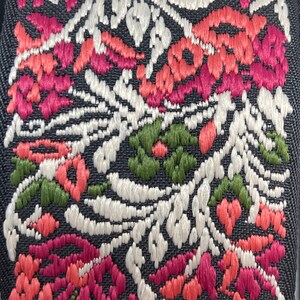 Puede incluir: Primer plano de una tela negra con un patr&oacute;n floral bordado en hilo blanco, rosa, rojo y verde.