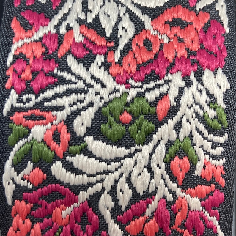 Puede incluir: Primer plano de una tela negra con un patr&oacute;n floral bordado en hilo blanco, rosa, rojo y verde.