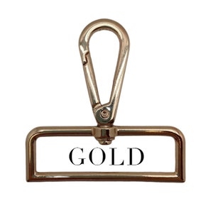 Puede incluir: Un cierre de metal dorado con una etiqueta rectangular que dice "GOLD" en letras negras.
