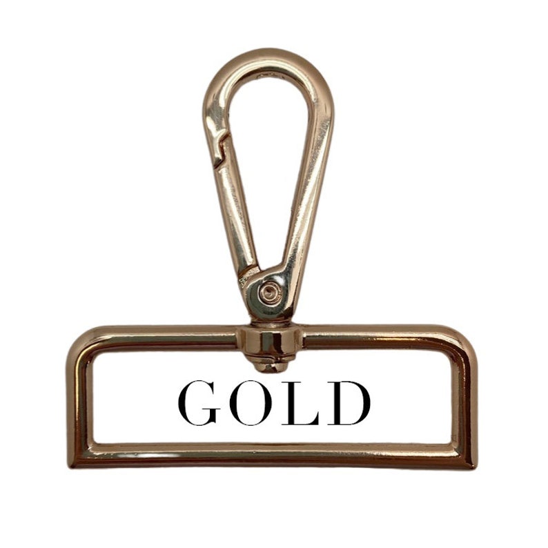 Puede incluir: Un cierre de metal dorado con una etiqueta rectangular que dice "GOLD" en letras negras.