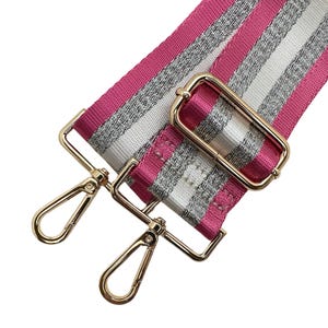 Peut inclure: Une bandouli&egrave;re de sac &agrave; rayures roses, argent&eacute;es et blanches avec une quincaillerie en m&eacute;tal dor&eacute;. La bandouli&egrave;re comporte deux mousquetons pivotants dor&eacute;s et une boucle rectangulaire dor&eacute;e. La bandouli&egrave;re est en tissu tiss&eacute;.