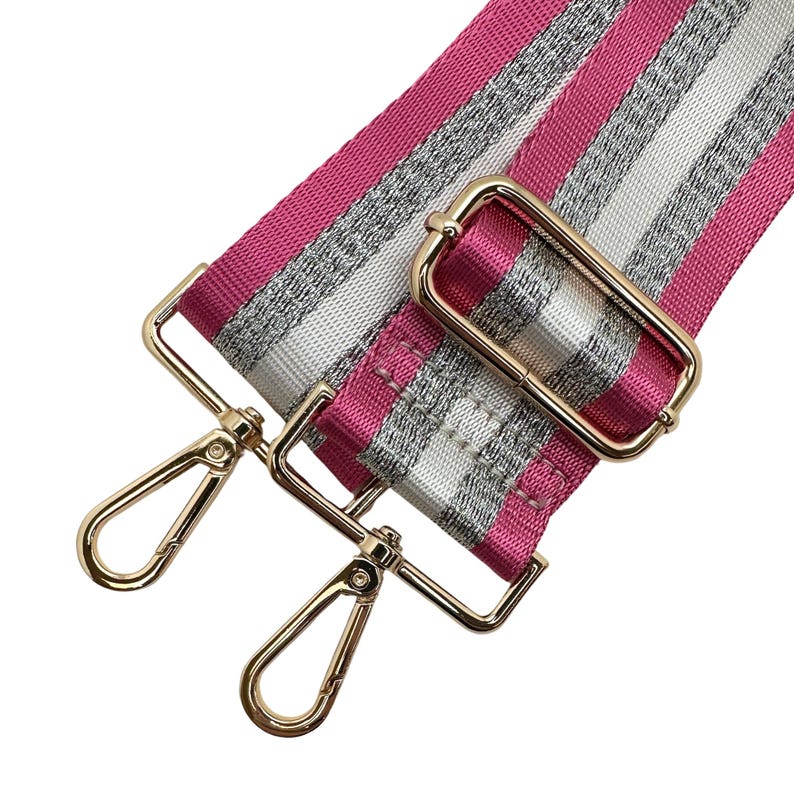 Peut inclure: Une bandouli&egrave;re de sac &agrave; rayures roses, argent&eacute;es et blanches avec une quincaillerie en m&eacute;tal dor&eacute;. La bandouli&egrave;re comporte deux mousquetons pivotants dor&eacute;s et une boucle rectangulaire dor&eacute;e. La bandouli&egrave;re est en tissu tiss&eacute;.
