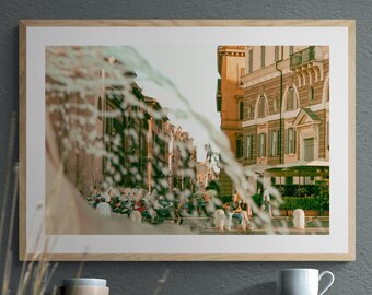 May include: A framed photograph of a European street scene, featuring buildings and people. The image is reflected in a water feature in the foreground. A wooden shelf below holds a mug and two small bowls.