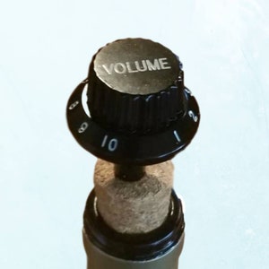 May include: A black volume knob with numbers 1 through 10. The knob is attached to a cork stopper.