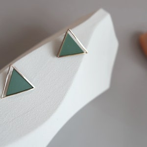 May include: A pair of green triangle earrings with a gold metal frame. The earrings are on a white surface.