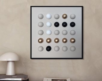 May include: A modern wall art piece featuring a grid of 25 spheres in various colors: white, black, gold, and gray. The artwork is framed in a black square frame and hangs on a neutral-toned wall. The room also includes a wooden nightstand, a lamp, and a bed.