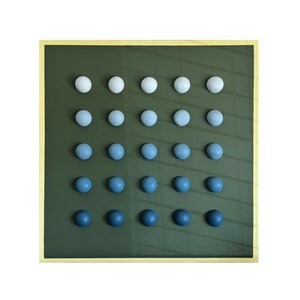 May include: A square artwork featuring a grid of 20 spherical objects. The spheres transition in color from white to deep blue, arranged on a dark green background. The artwork is framed with a gold border.