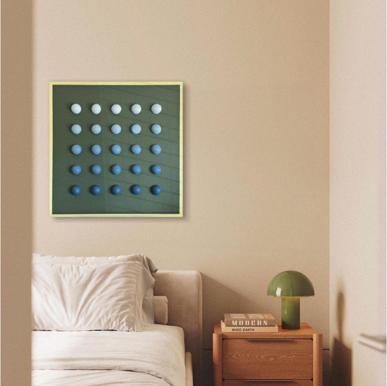 May include: A framed wall art piece featuring a grid of gradient blue and white spheres on a dark green background. The artwork is in a gold frame and hangs above a bed with a white comforter. A green mushroom lamp sits on a wooden nightstand.