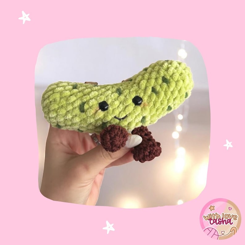 May include: A crocheted green pickle toy with a smiling face and brown feet. The pickle is made from a soft, textured yarn and has small, dark green spots. A charming, handmade item.