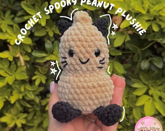 Puede incluir: Un peluche de cacahuete tejido a ganchillo en color beige con orejas y pies negros, con ojos y boca bordados en negro. El texto CROCHET SPOOKY PEANUT PLUSHIE aparece arqueado encima, con estrellas blancas y un logotipo circular rosa.