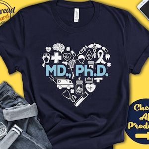 May include: A navy blue t-shirt with a white heart design featuring medical symbols and the text "MD, Ph.D."