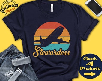May include: Navy blue t-shirt with a retro design featuring an airplane silhouette against a sunset backdrop. The word "Stewardess" is written in a vintage font below the plane. The shirt also has the text "Check All Products".