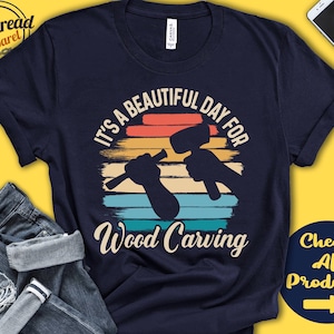 Puede incluir: Una camiseta azul marino con un gr&aacute;fico de estilo vintage que dice "Es un hermoso d&iacute;a para tallar madera". El gr&aacute;fico presenta una puesta de sol con una mano sosteniendo un mazo y un cincel.