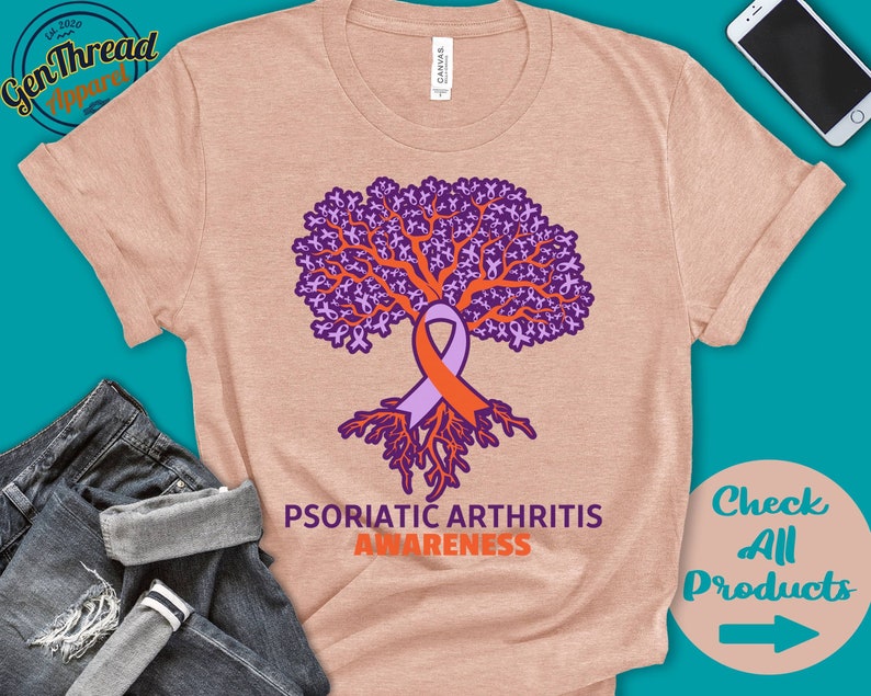 May include: A light pink t-shirt with a purple tree made of ribbons. The tree has orange roots and a purple and orange ribbon tied around the trunk. The text "Psoriatic Arthritis Awareness" is printed below the tree.