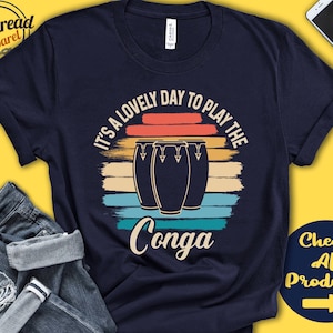 Puede incluir: Una camiseta azul marino con un gráfico de estilo vintage de tres tambores de conga y el texto "Es un día precioso para tocar la conga".