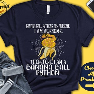 Może przedstawiać: Granatowa koszulka z napisem "Banana Ball Pythons Are Awesome. I Am Awesome. Therefore, I Am A Banana Ball Python." Zawiera grafikę węża w okularach przeciwsłonecznych wychodzącego ze skórki banana.