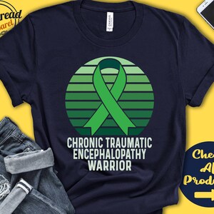 May include: A navy blue t-shirt with a green ribbon and a sunset design. The text "Chronic Traumatic Encephalopathy Warrior" is printed on the shirt.