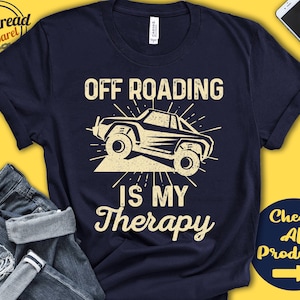 Könnte beinhalten: Ein marineblaues T-Shirt mit dem Text "Off Roading is my Therapy" in Weiß. Eine Schwarzweißillustration eines Jeeps befindet sich über dem Text.