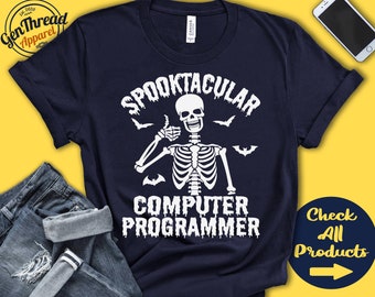 Könnte beinhalten: Marineblaues T-Shirt mit weißem Skelett-Grafik und dem Text "Spooktacular Computer Programmer". Das Design beinhaltet Fledermäuse und einen Daumen hoch. Das T-Shirt liegt gefaltet neben einer Jeans und einem Smartphone.