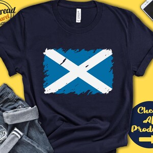 May include: A navy blue t-shirt with a distressed white and blue Scottish flag design. The text "Check All Products" with a right arrow is in the bottom right corner of the image.