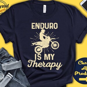 May include: A navy blue t-shirt featuring a graphic of a dirt bike and the text "Enduro is my therapy".
