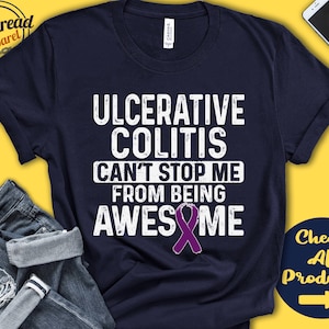 May include: A navy blue t-shirt with white text that reads "Ulcerative Colitis Can't Stop Me From Being Awesome". A purple ribbon is below the text.