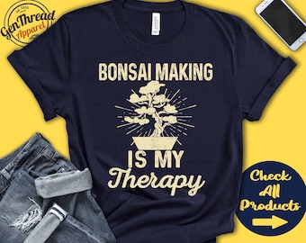 May include: A navy blue t-shirt with the text "Bonsai Making is My Therapy" in white. A stylized image of a bonsai tree in a pot is above the text.