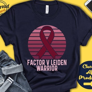 May include: A navy blue t-shirt with a pink and red sunset graphic and a burgundy ribbon. The text "Factor V Leiden Warrior" is printed in white below the graphic.