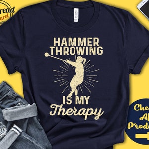 May include: A navy blue t-shirt with a white graphic of a person throwing a hammer. The text "Hammer Throwing is My Therapy" is printed in white on the shirt.
