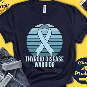 May include: A navy blue t-shirt with a light blue ribbon and a retro-style sunset graphic. The text "Thyroid Disease Warrior" is printed below the graphic.