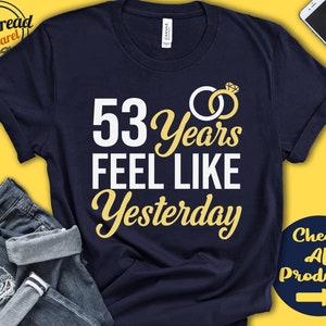 May include: Navy blue t-shirt with white text that reads "53 Years Feel Like Yesterday" and a gold ring with a diamond graphic. The text is in a stylized font.
