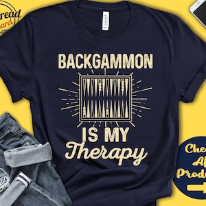 May include: A navy blue t-shirt with the text "Backgammon is my therapy" in white. A stylized image of a backgammon board is above the text.