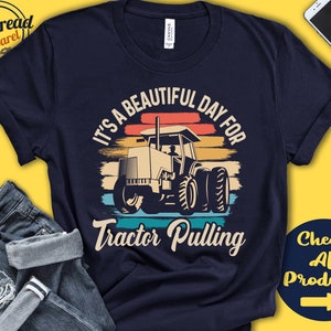 May include: A navy blue t-shirt with a vintage-style graphic of a tractor pulling. The graphic features a sunset background with the text "It's a beautiful day for tractor pulling".