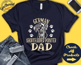 Può includere: Una maglietta blu navy con il testo "German Shorthaired Pointer Dad" in lettere bianche e gialle. Sopra il testo c'è un'illustrazione in bianco e nero di un cane Bracco tedesco a pelo corto. Ci sono impronte di zampe gialle intorno al cane.