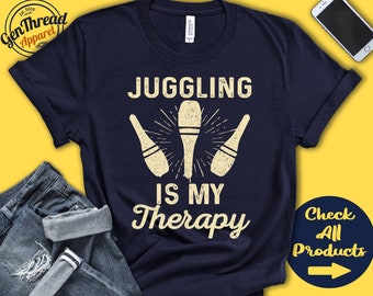 Könnte beinhalten: Ein marineblaues T-Shirt mit dem Text "Juggling is my therapy" in Weiß. Der Text ist von drei weißen Jonglierkeulen umgeben.