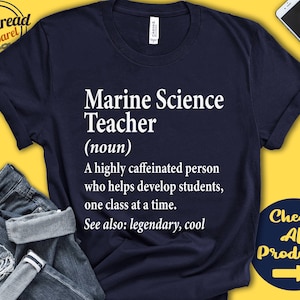 以下が含まれることがあります： 「Marine Science Teacher (noun) A highly caffeinated person who helps develop students, one class at a time. See also: legendary, cool」と白文字で書かれたネイビーブルーのTシャツ