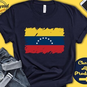 May include: A navy blue t-shirt with a distressed, faded image of the Venezuelan flag. The flag is yellow, blue, and red with a crescent of white stars. The text "Check All Products" is on a blue background with a white arrow pointing to the right.
