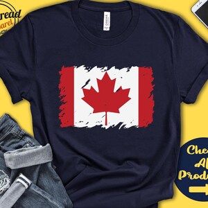 May include: A navy blue t-shirt with a distressed Canadian flag design. The flag features a red maple leaf on a white background with red stripes on the sides. The text "Check All Products" with a right arrow is in the bottom right corner.
