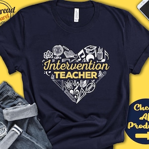 Puede incluir: Camiseta azul marino con un diseño de corazón blanco que presenta varios iconos relacionados con la escuela y el texto "Intervention Teacher" en amarillo.