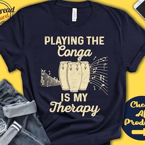 May include: Navy blue t-shirt with the text "Playing the Conga is my Therapy" and a graphic of three conga drums with musical notes.