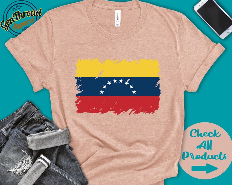May include: A light pink t-shirt with a distressed, faded image of the Venezuelan flag. The flag is yellow, blue, and red with a white star in the center of the blue stripe. The t-shirt is a casual style with short sleeves and a crew neck.