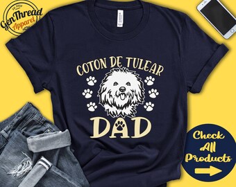 May include: A navy blue t-shirt with the text "Coton de Tulear Dad" in yellow. A white silhouette of a Coton de Tulear dog is in the centre of the shirt. There are paw prints around the dog and text.