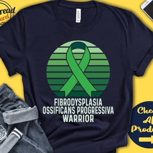 Peut inclure: Un t-shirt bleu marine avec un ruban vert et un design de coucher de soleil. Le texte "Fibrodysplasia Ossificans Progressiva Warrior" est imprimé sur le t-shirt.