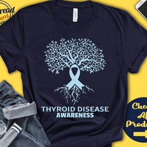 Puede incluir: Una camiseta azul marino con un diseño de árbol de cinta azul claro. El texto "Thyroid Disease Awareness" está impreso debajo del árbol.