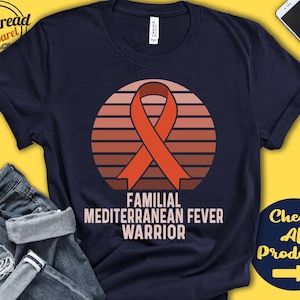 Op de afbeelding: Een marineblauw t-shirt met een rood lint en een zonsondergangafbeelding. De tekst "Familial Mediterranean Fever Warrior" is op het t-shirt gedrukt.