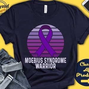 May include: A navy blue t-shirt with a purple ribbon and a sunset design. The text "Moebius Syndrome Warrior" is printed on the shirt.