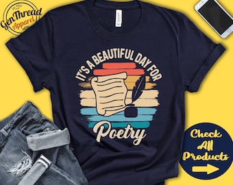 Puede incluir: Una camiseta azul marino con un diseño gráfico de estilo vintage que presenta un rollo, una pluma y el texto "Es un hermoso día para la poesía".