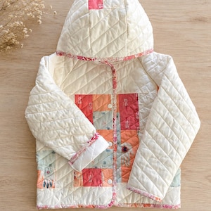 May include: A quilted hooded jacket featuring a cream-colored base with diagonal stitching. The front panel displays a patchwork design of rectangular fabric blocks in shades of pink, orange, and light green, finished with a floral-patterned trim.
