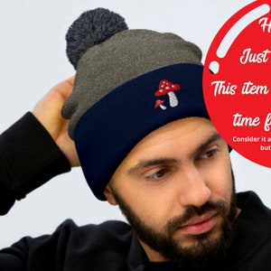 May include: A man wearing a gray and navy blue beanie with a mushroom graphic and a pom pom on top. The beanie has the text "Ho, ho, ho Just so you know This item won't make it in time for Christmas. Consider it a Christmas miracle if it does, but not an expectation."
