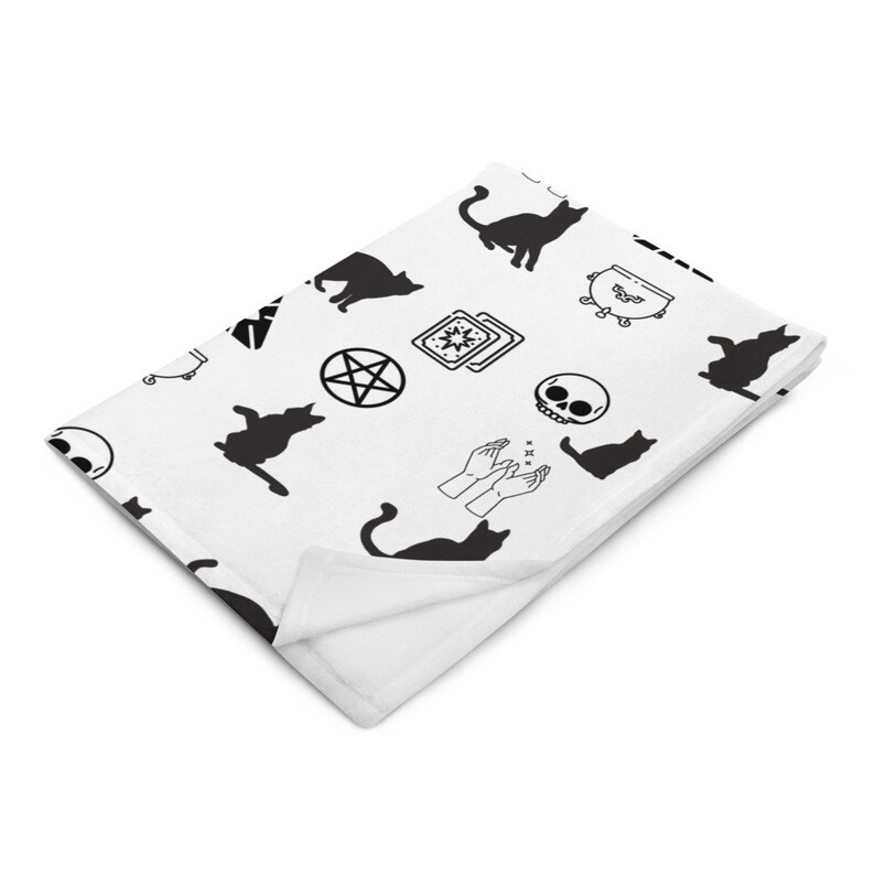 May include: White throw blanket with a black and white pattern of various witchy symbols including cats, a cauldron, a pentagram, tarot cards, a skull, and a pair of hands casting a spell.
